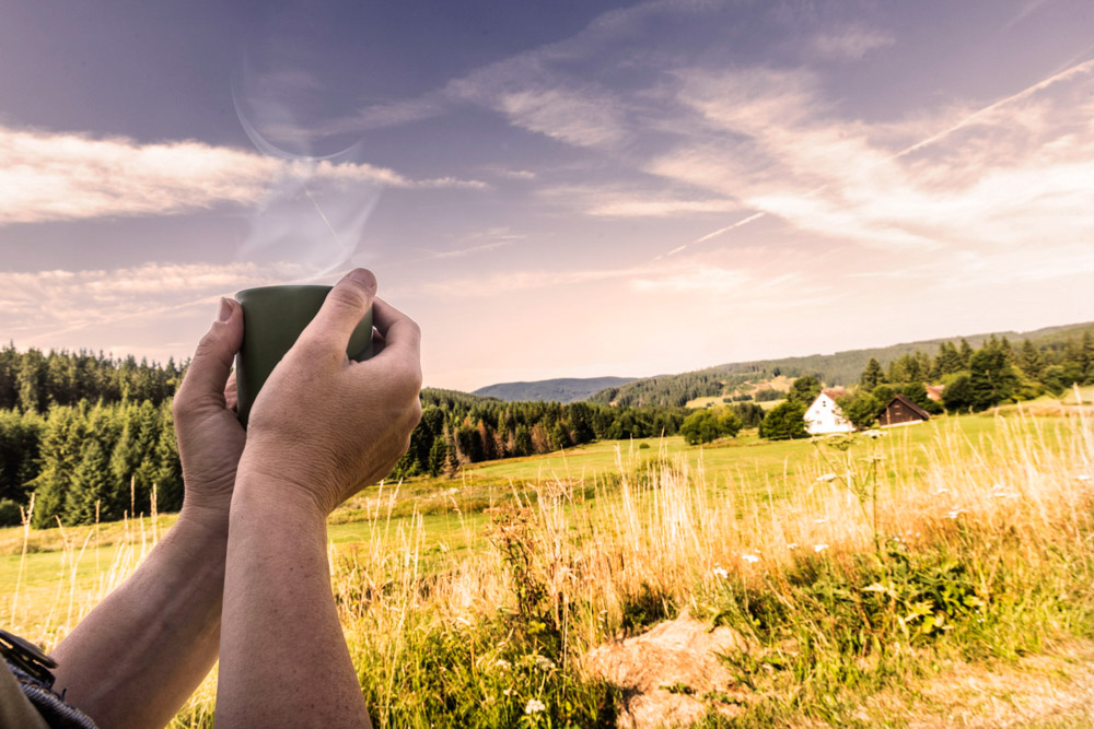 Person mit Tasse in der Hand vor einer Wiese